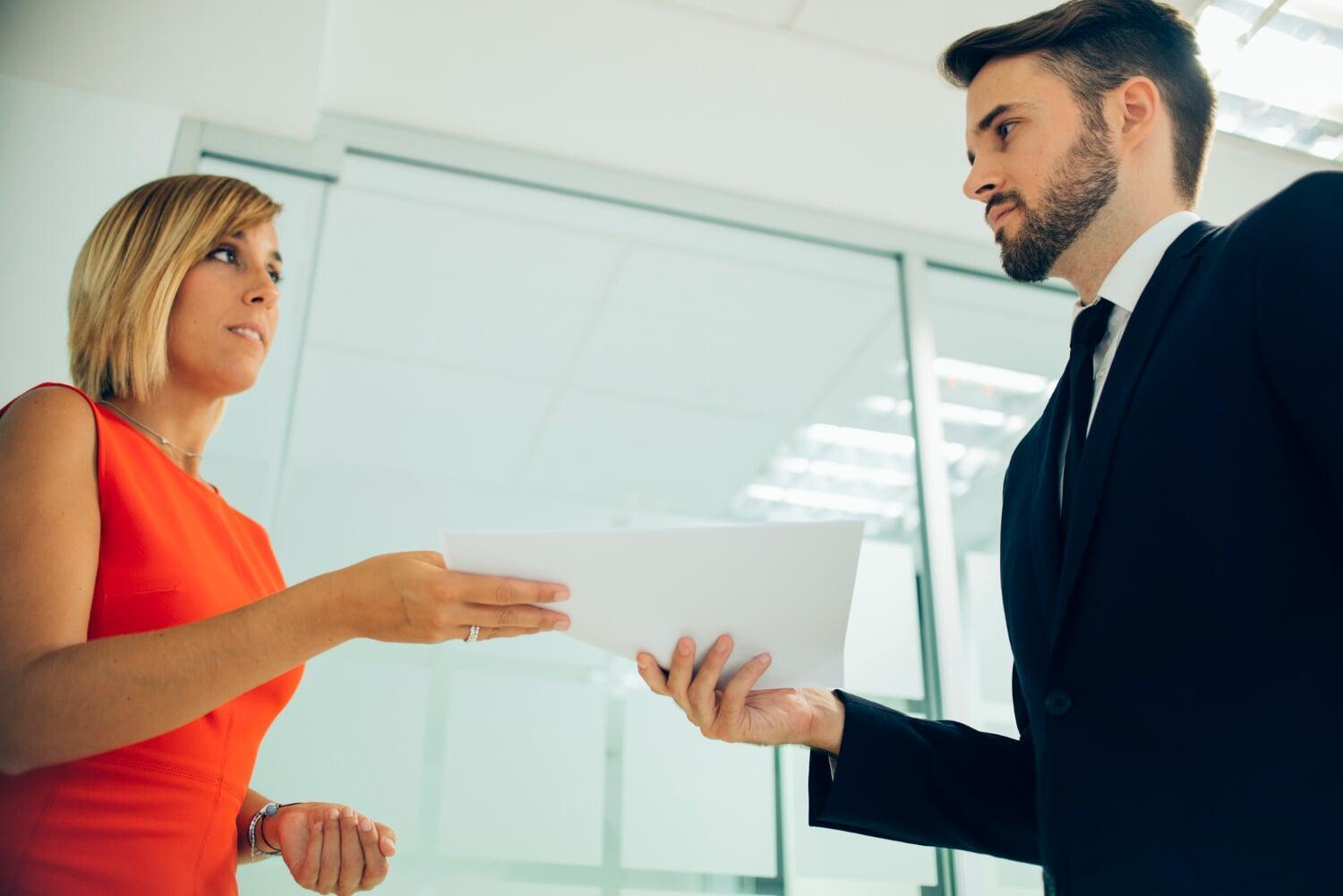 Mulher entrega documento a homem de terno em ambiente corporativo moderno