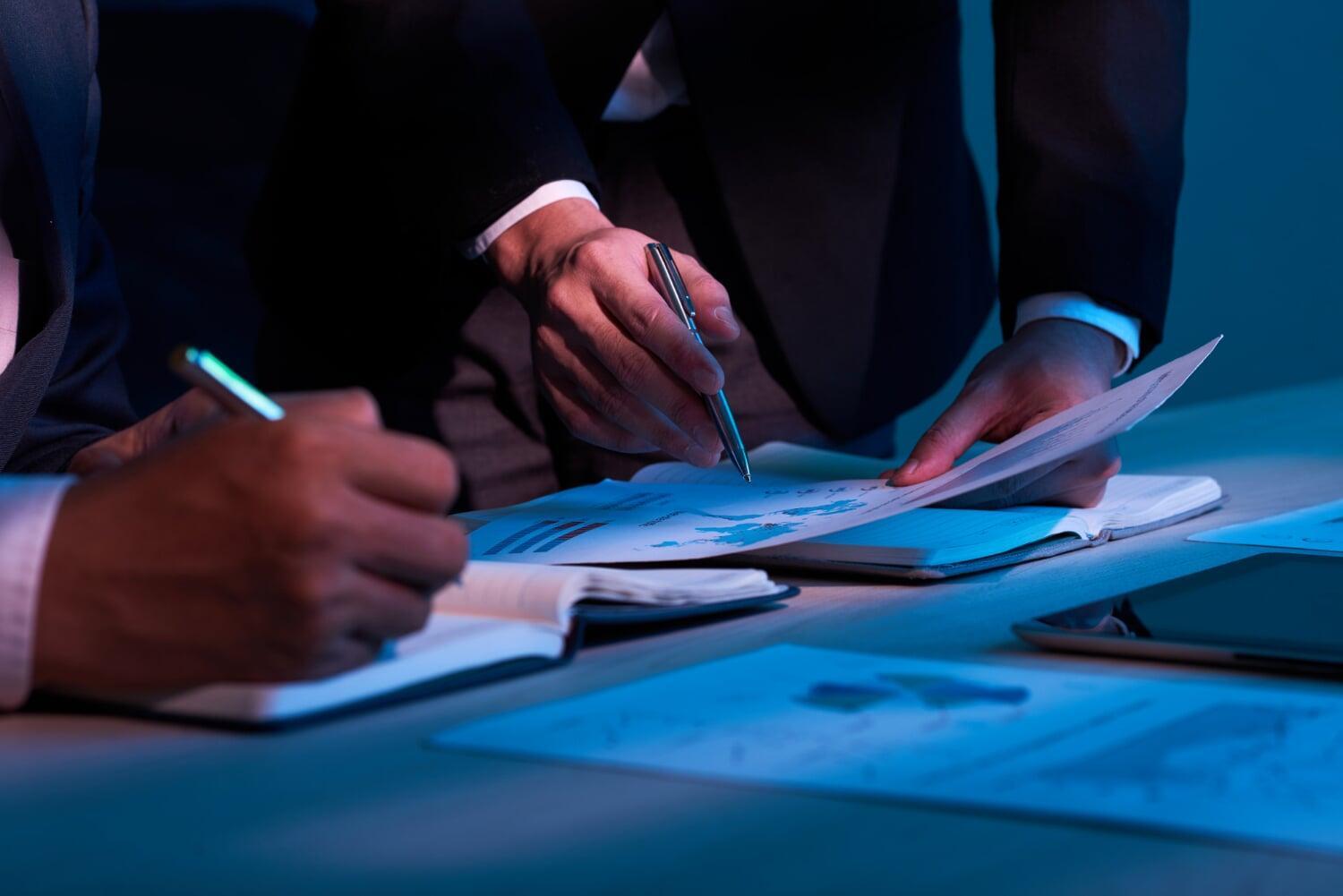Duas pessoas analisando documentos financeiros com gráficos em uma reunião de negócios