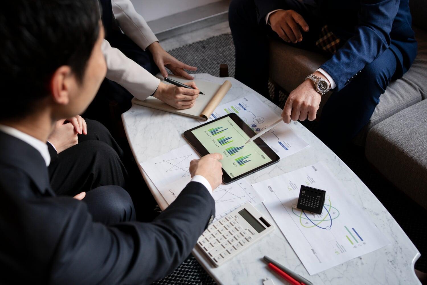 Empresários reunidos em mesa de reunião analisando gráficos em um tablet