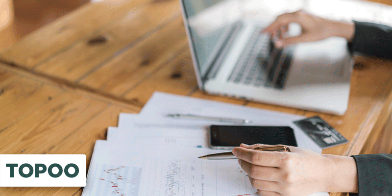 Profissional trabalhando com notebook e analisando gráficos financeiros impressos