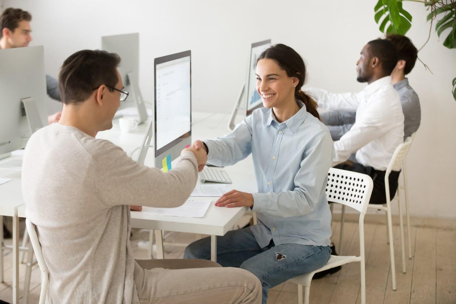 Pessoas em ambiente de trabalho apertando as mãos em frente ao computador