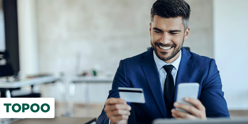 Homem de terno segurando cartão de crédito e celular com expressão de felicidade